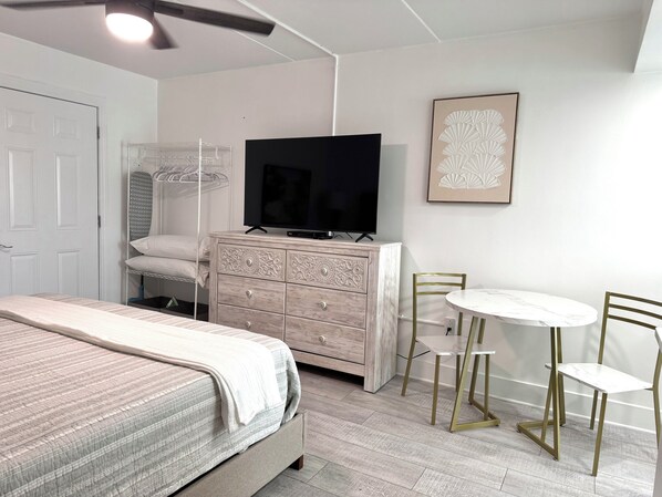A bedroom with a bed, dresser, TV, and a small dining area with chairs and a table. - Beachview 214 remodeled efficiency studio condo with King bed (Gulf Shores)