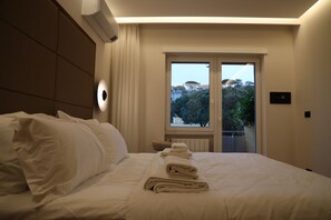 A hotel room with a bed, a window with a view of trees and buildings, and a wall-mounted air conditioning unit. - The Romex (Rome)