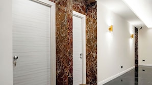 A hallway with marble walls and doors, a polished floor, and wall-mounted lighting fixtures. - The Romex (Rome)