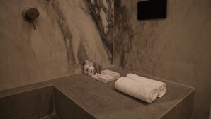 A bathroom with a marble wall, a towel on the counter, and toiletries. - The Romex (Rome)