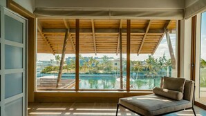 Ein Zimmer mit großem Fensterblick auf Pool und Palmen, einer Holzbalkendecke und einem gepolsterten Sessel.