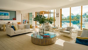 Ein geräumiges Wohnzimmer mit großem Fenster mit Blick auf einen Pool, einem runden Couchtisch mit Büchern und einem weißen Sofa.
