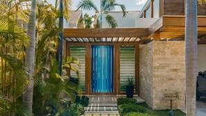 Ein modernes Haus mit einer Holzpergola, einer blauen Tür und einer Steinmauer.