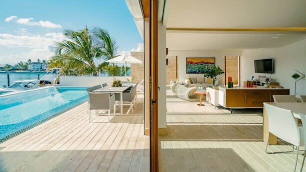 Ein modernes Wohnzimmer mit großem Fenster, das auf einen Pool und Palmen blickt.