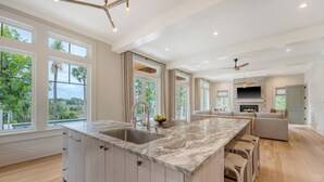 Una cocina moderna con encimera de mármol, una isla grande con taburetes de bar, horno empotrado y vistas al exterior.
