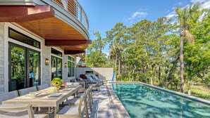 Zona junto a la piscina con terraza de madera, mobiliario exterior y vistas a la piscina.