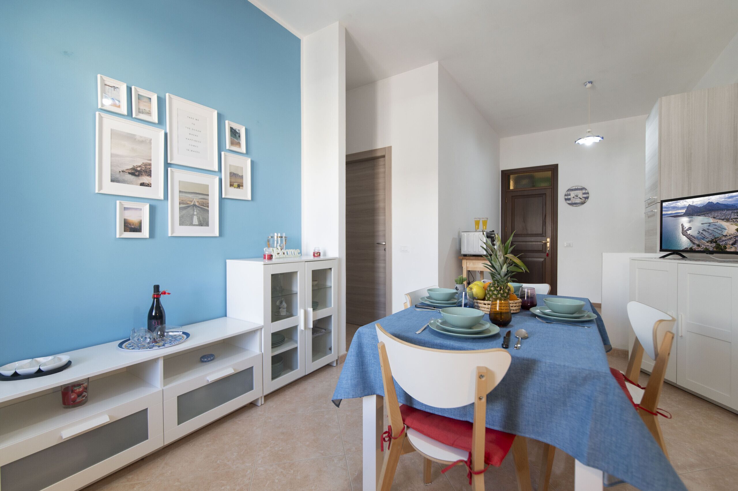 Un coin repas avec une nappe bleue, des chaises blanches et un buffet blanc aux portes vitrées.