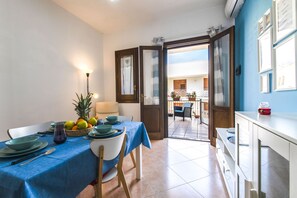 A dining area with a table set for four, a fruit bowl, and a lamp. - Appartamento La Loggetta (San Vito Lo Capo)