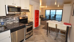 A modern kitchen with stainless steel appliances, a dining area with a white table and bar stools, and a balcony with a view of the sea. - Edgewater House - Ocean Front Units With Spectacular Views! (Rehoboth Beach)