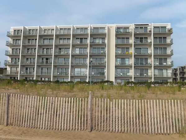 Een meerlaags hotel met balkons, een zandig voorgronddeel en een heldere lucht.