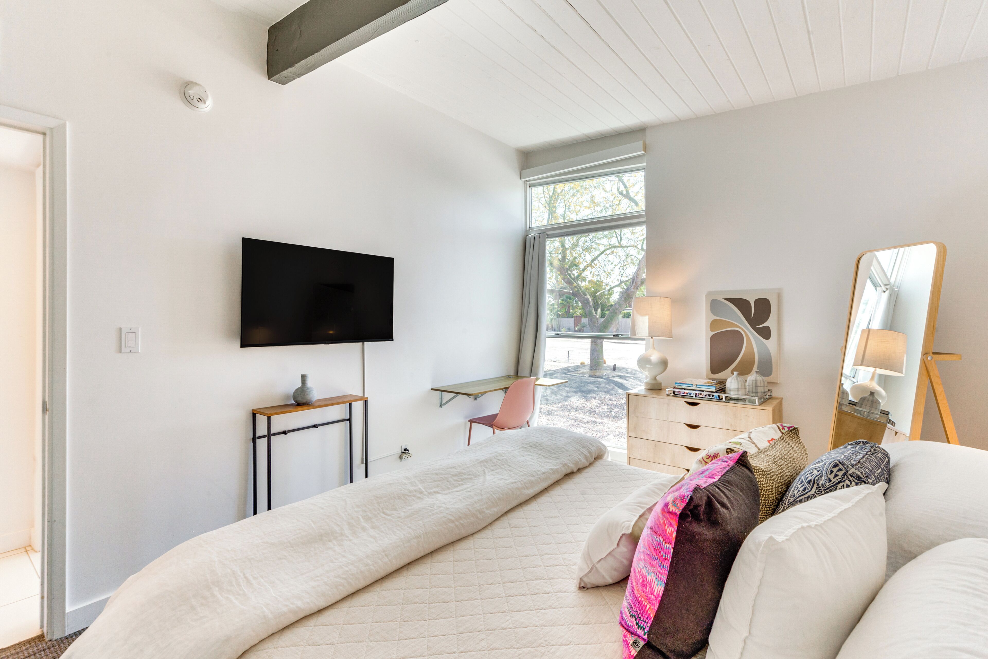 A bedroom with a bed, a TV, a desk, and a window.