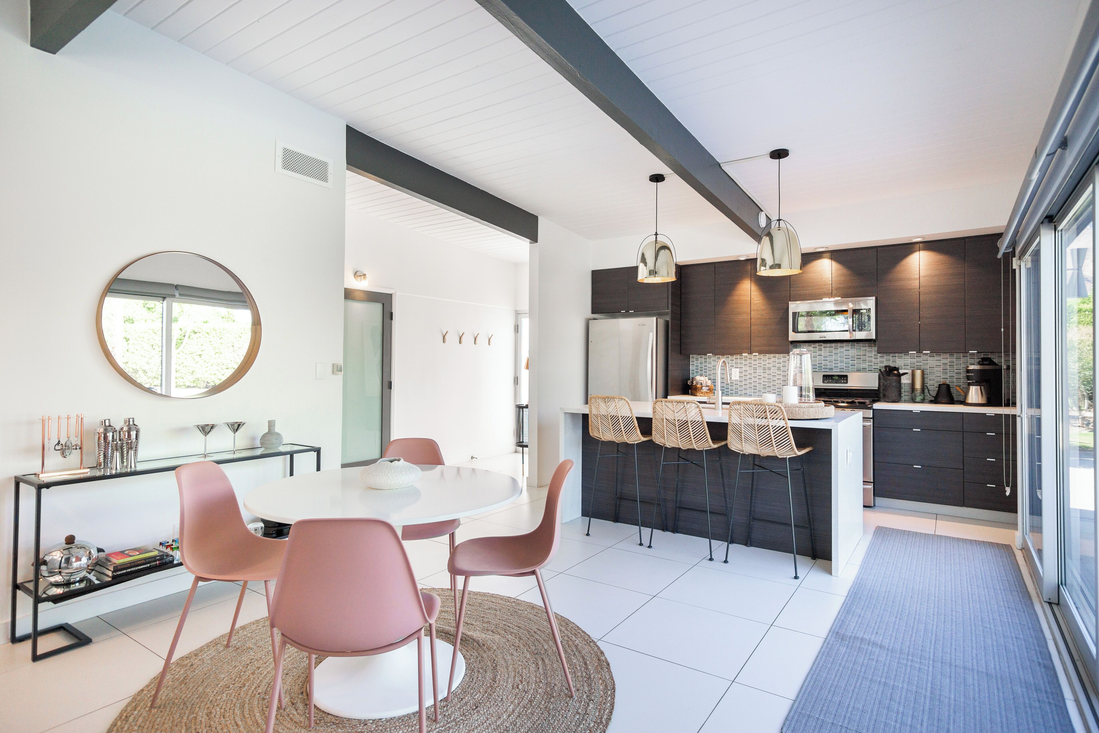A modern kitchen with dark cabinetry, a central island, and a dining area with a round table and pink chairs.