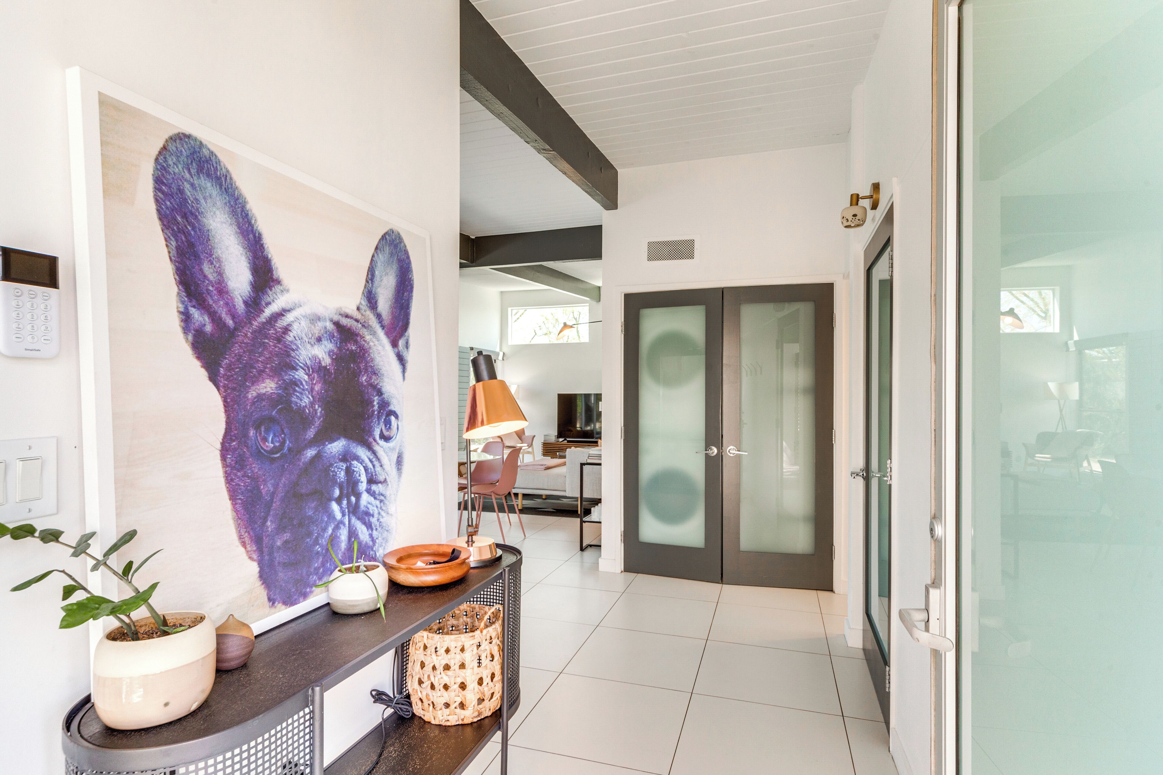 A modern interior with a large wall art of a dog, a dining area with a lamp, and a glass door leading to another room.