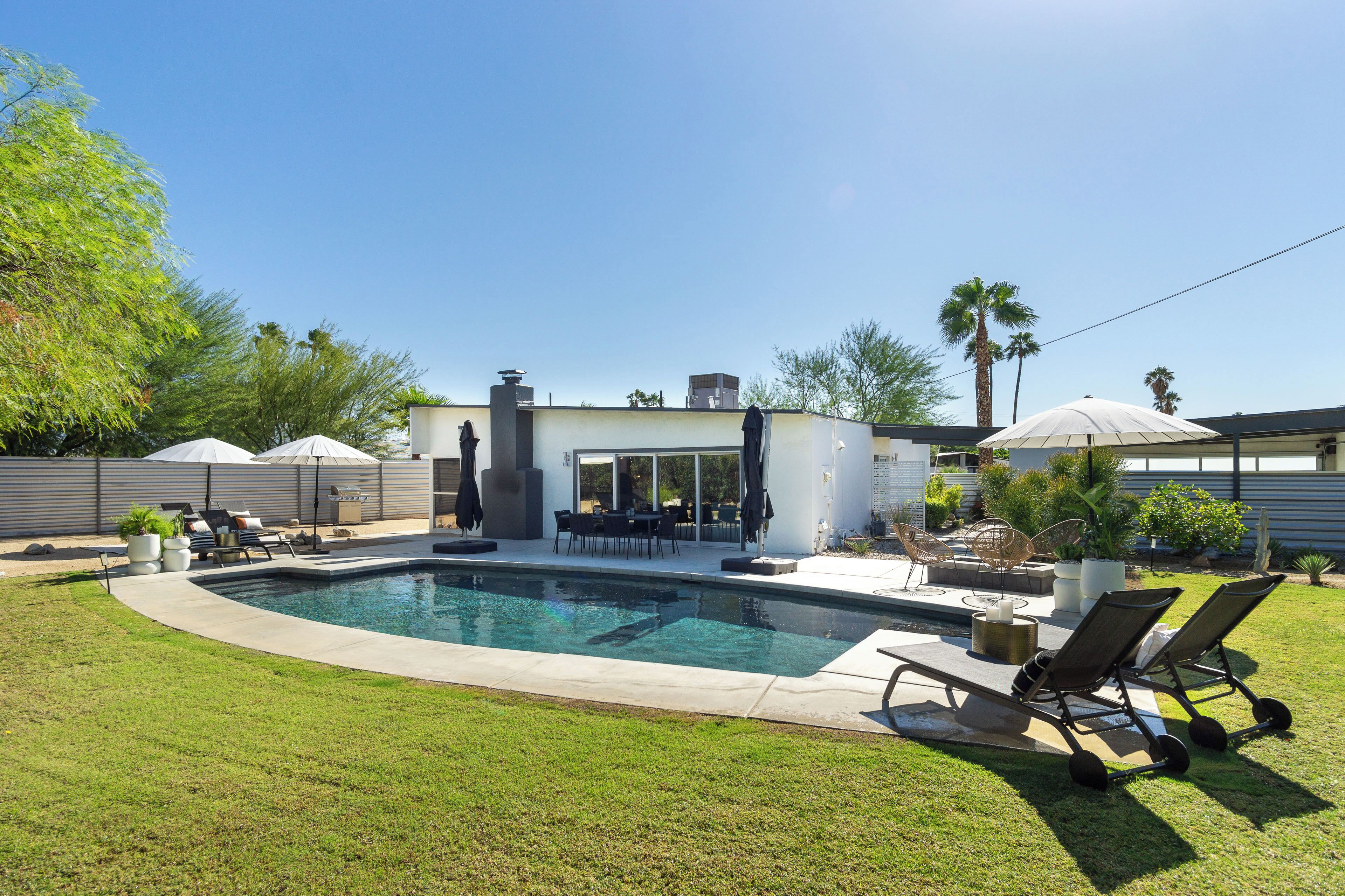 A backyard with a swimming pool, outdoor furniture, and a patio area.