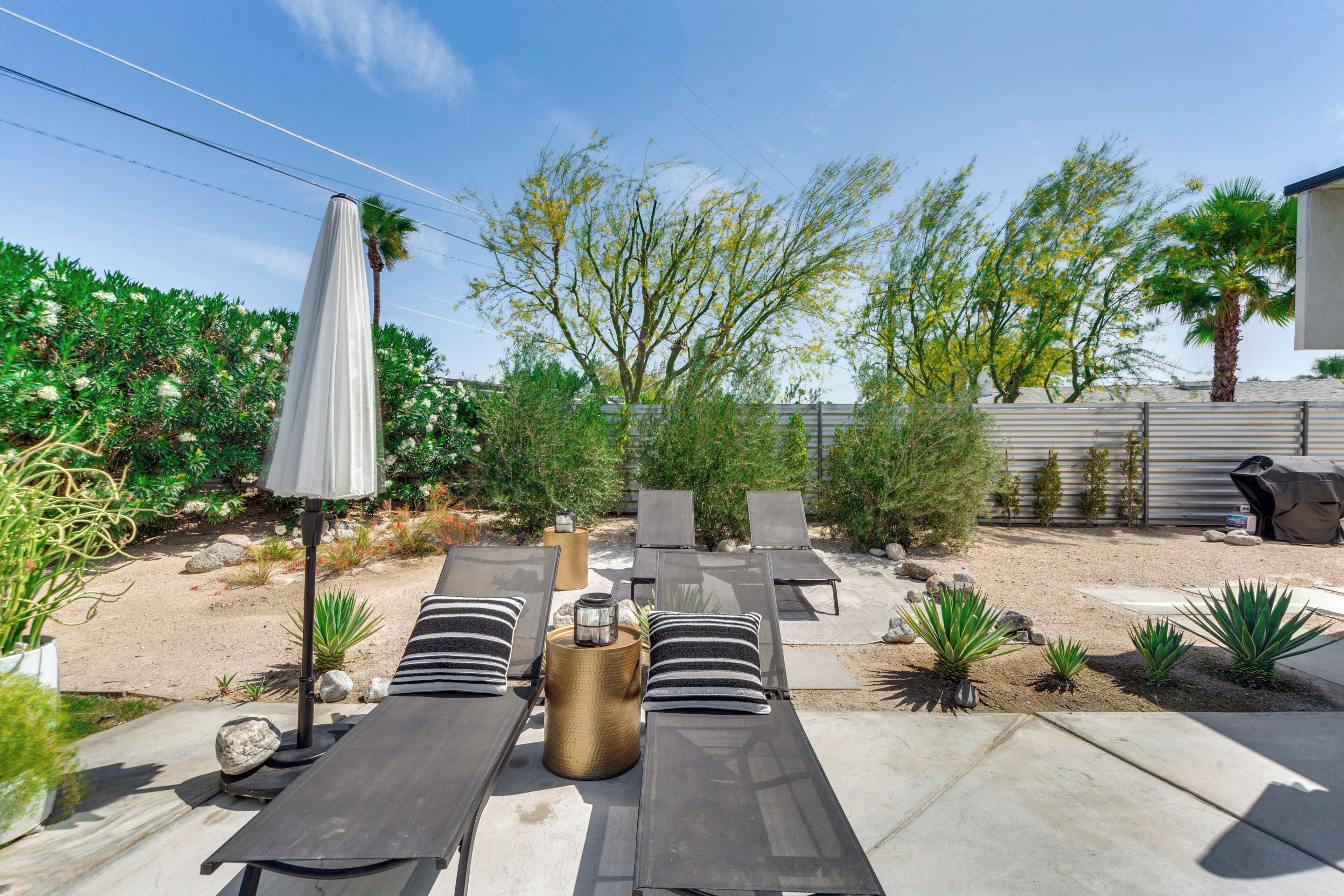 A patio area with sun loungers, a table with a glass top, and a grill.