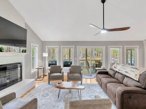 A spacious living room with a fireplace, comfortable seating, and large windows offering a view of the outdoors.