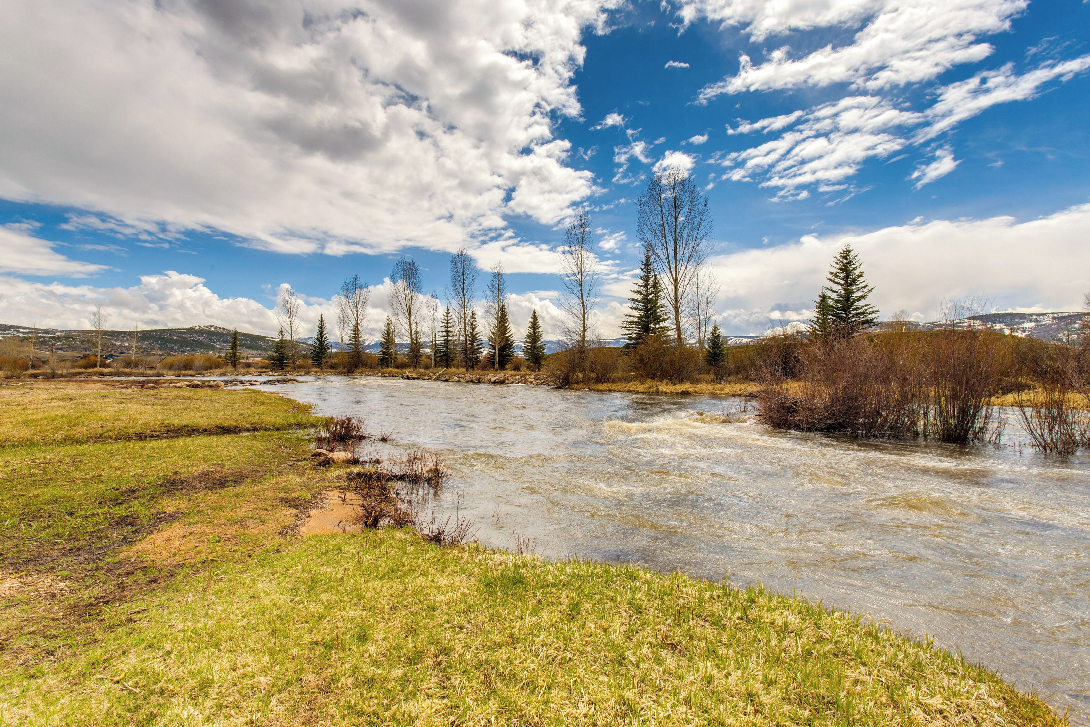 A river flowing through a grassy landscape with trees and hills in the background.