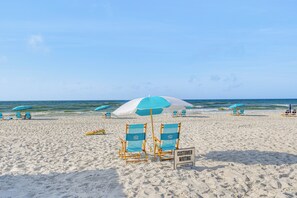 Une plage avec des chaises et des parasols bleus, et un panneau indiquant : « ATTENTION, GRANDE VAGUE À L’APPROCHE ».