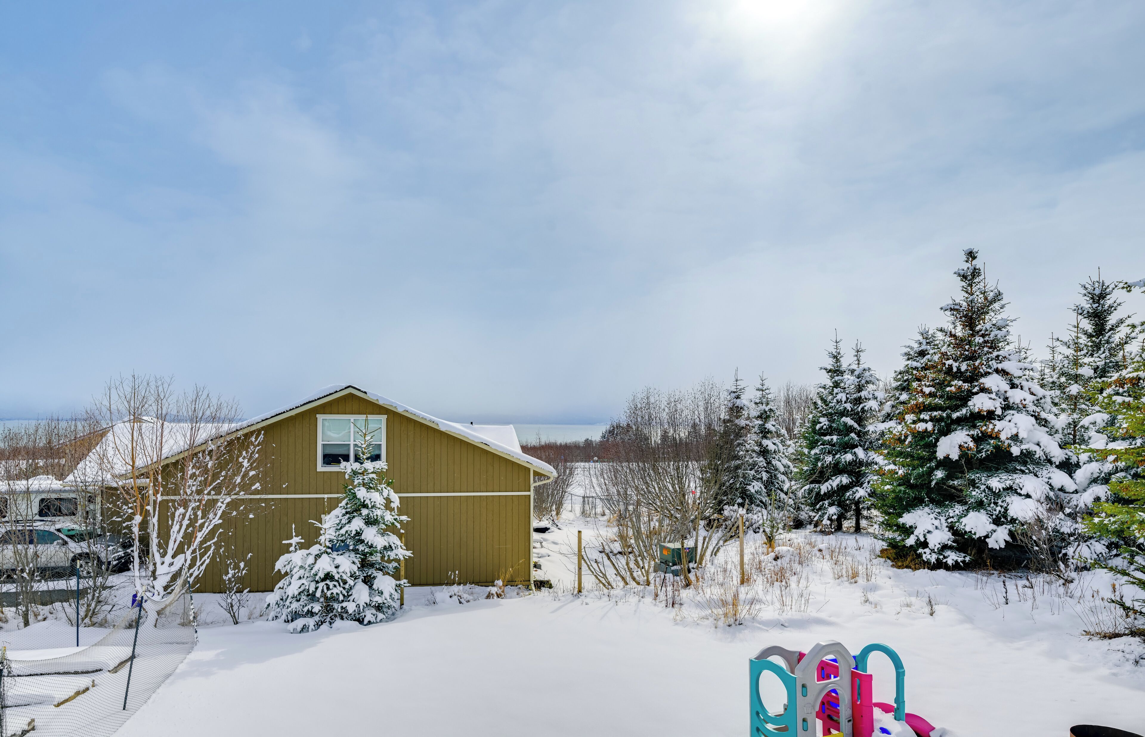 Una casa de madera con garaje, rodeada de árboles cubiertos de nieve y un cielo despejado.