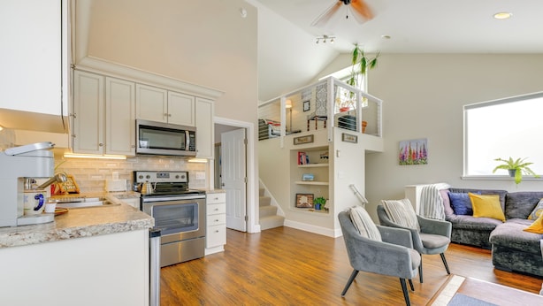 A modern kitchen with built-in appliances, a dining area with a gray sofa and armchairs, and a staircase leading to a loft bedroom. - Scenic & Cozy 'sweet Northern Comfort' in Homer! (Homer)