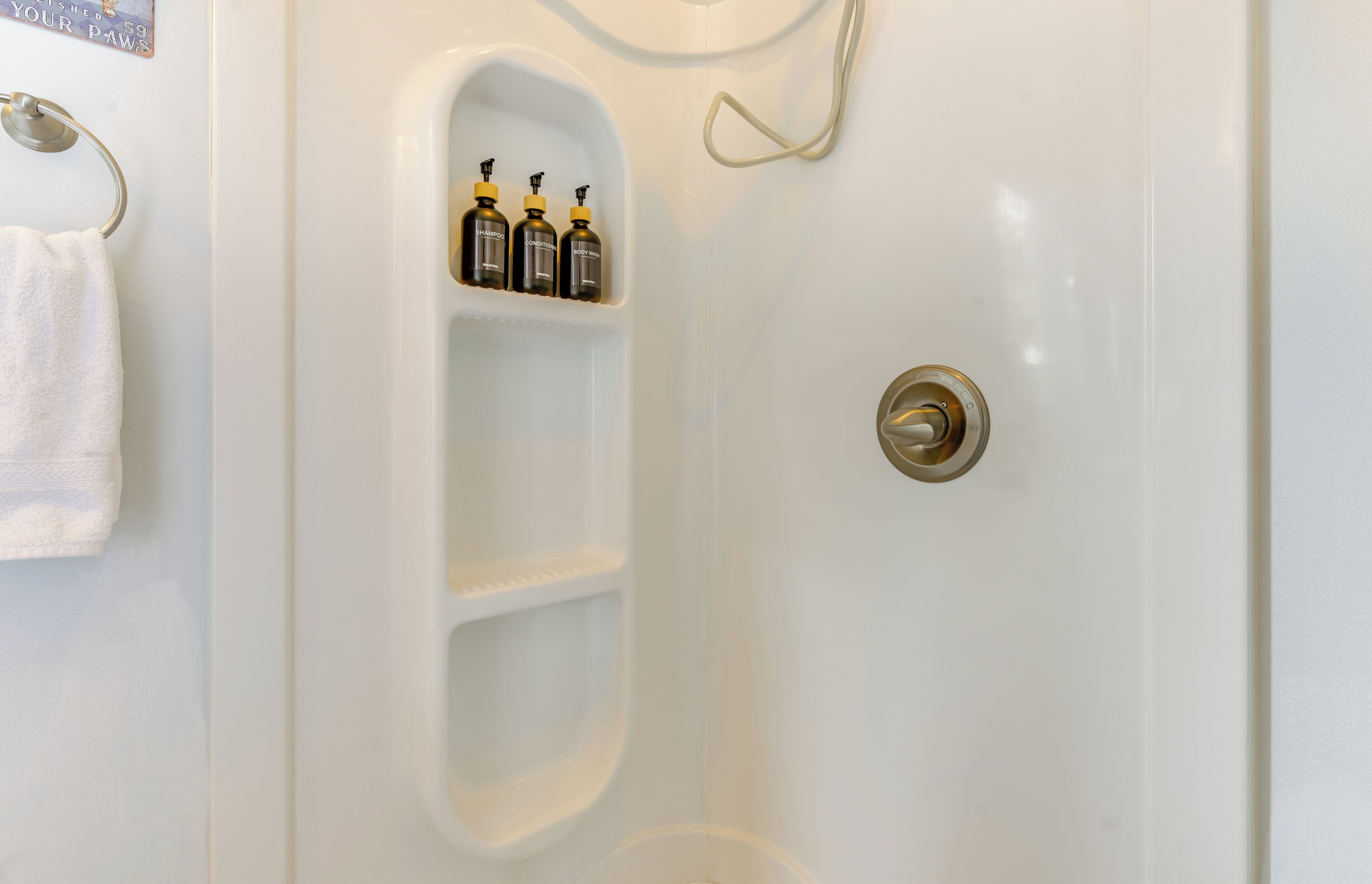 A bathroom with a white bathtub, a towel rack, and a shelf with three bottles.