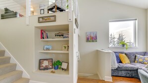 A staircase with a built-in bookshelf, a gray sofa with patterned cushions, and a window with a view of trees. - Scenic & Cozy 'sweet Northern Comfort' in Homer! (Homer)