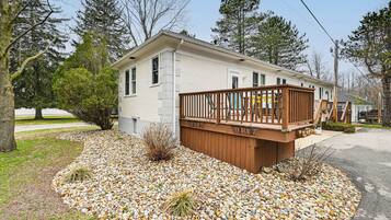 Une maison de plain-pied dotée d’une terrasse en bois, entourée d’une allée en gravier et de petits arbustes.