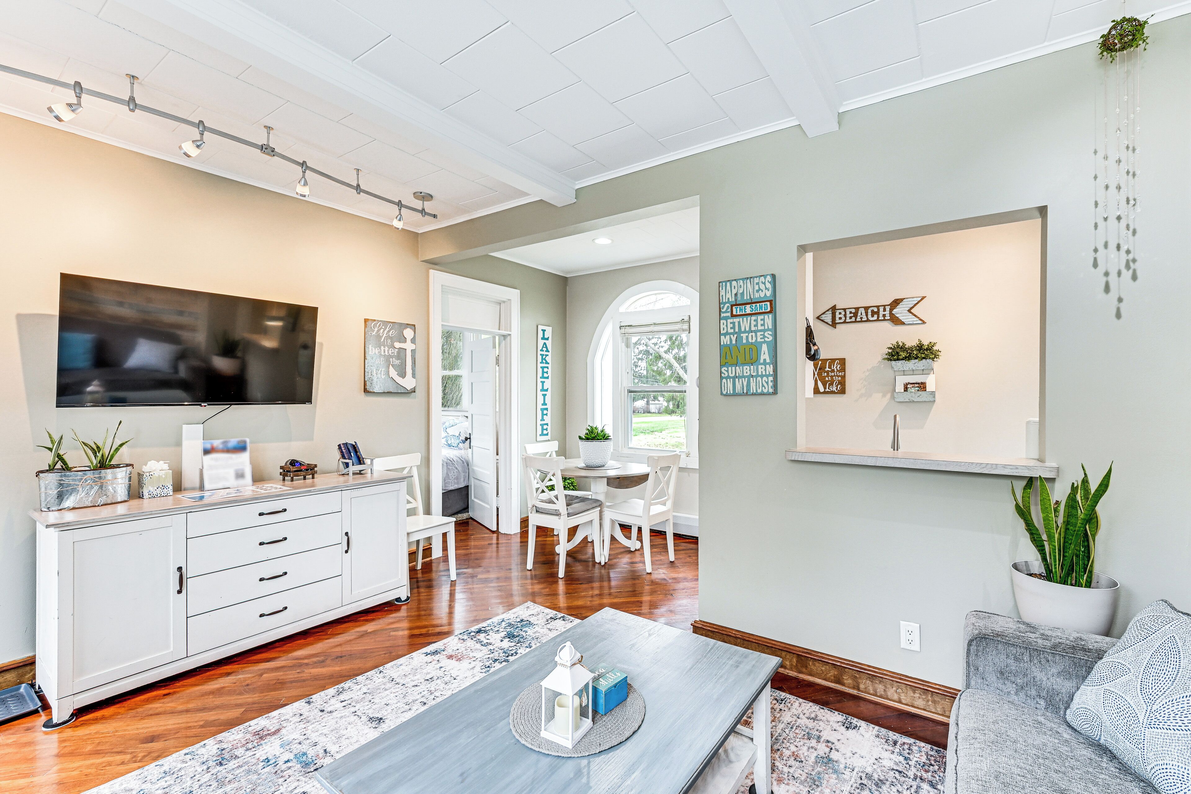 A modern living room with a flat-screen TV, white furniture, and a dining area with a table and chairs.