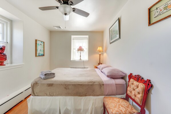Une chambre à coucher avec un lit, une chaise, un ventilateur de plafond, une fenêtre et une lampe.