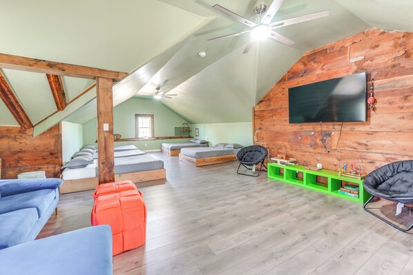 A spacious loft with a high ceiling, wooden beams, a large TV mounted on the wall, and a green storage unit. - Historic Manor 3 Mi to Shawnee Mtn! Pet Friendly (East Stroudsburg)
