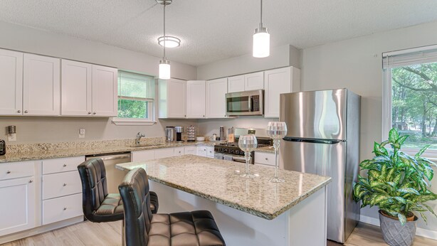 A modern kitchen with white cabinets, granite countertops, stainless steel appliances, and a central island with bar stools. - 11 Mi to Beaches: Peaceful Foley Home w/ Yard (Foley)