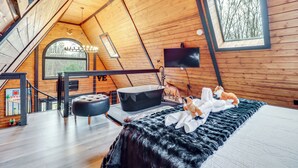 Ein gemütliches Schlafzimmer unter dem Dach mit einem großen Fenster, einer schwarzen Badewanne und komfortabler Bettwäsche.