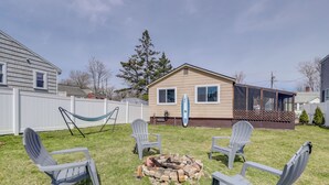 Ein Garten mit Feuerstelle, vier Adirondack-Stühlen und einer Hängematte.