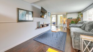 Ein modernes Wohnzimmer mit einem grauen Sofa, einem blauen Teppich mit Muster und einem an der Wand befestigten Fernseher.