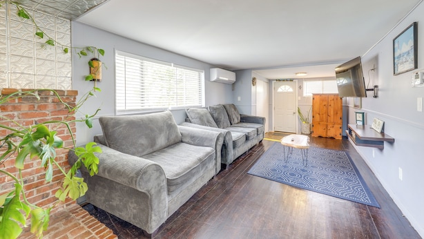 Ein Wohnzimmer mit zwei grauen Sofas, einem kleinen Tisch, einem blauen Teppich, einer Ziegelwand und einem Holzkasten.