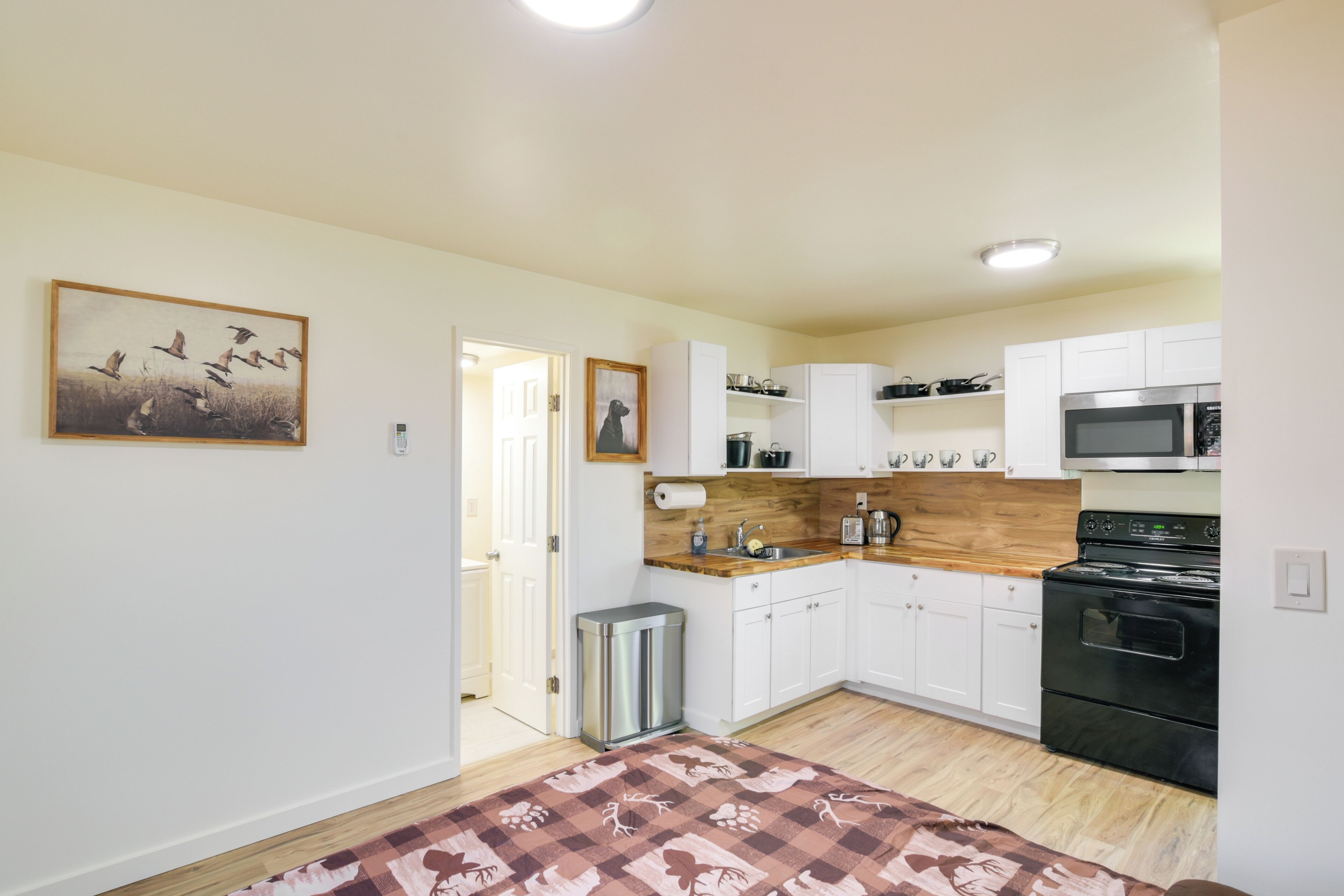 A modern kitchen with white cabinets, a wooden countertop, a stainless steel trash can, and a black stove.