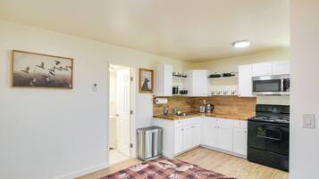 Una cocina moderna con armarios blancos, encimera de madera, cubo de basura de acero inoxidable y estufa negra.