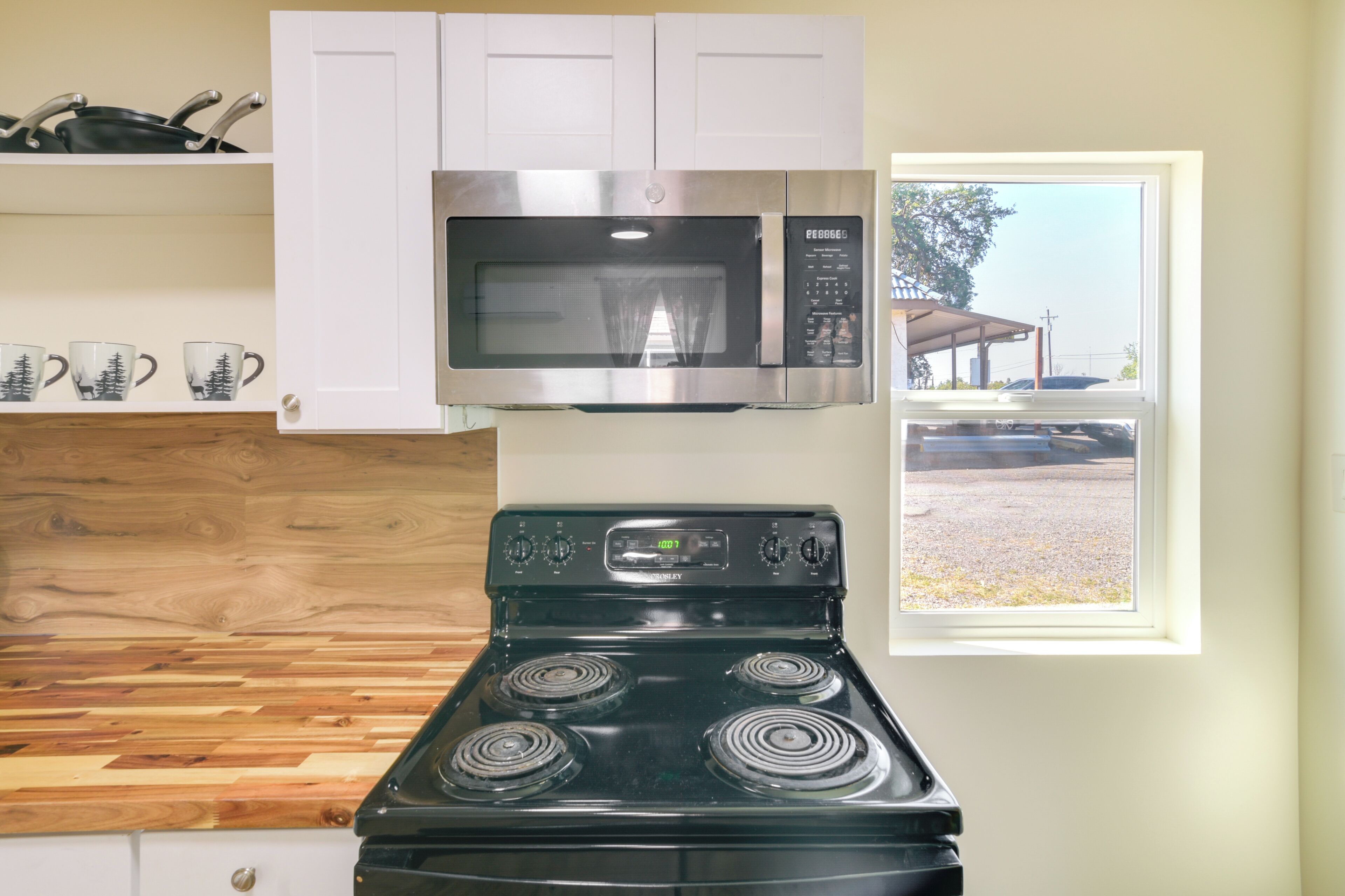 A kitchen with a black stove, a microwave above it, and a window with a view of a parking lot.