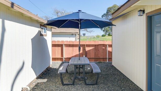A patio area with a picnic table and umbrella, surrounded by a wooden fence and a building with a door and window. - Studio 2 Mi to Feather River: Bring Your Pet! (Oroville)