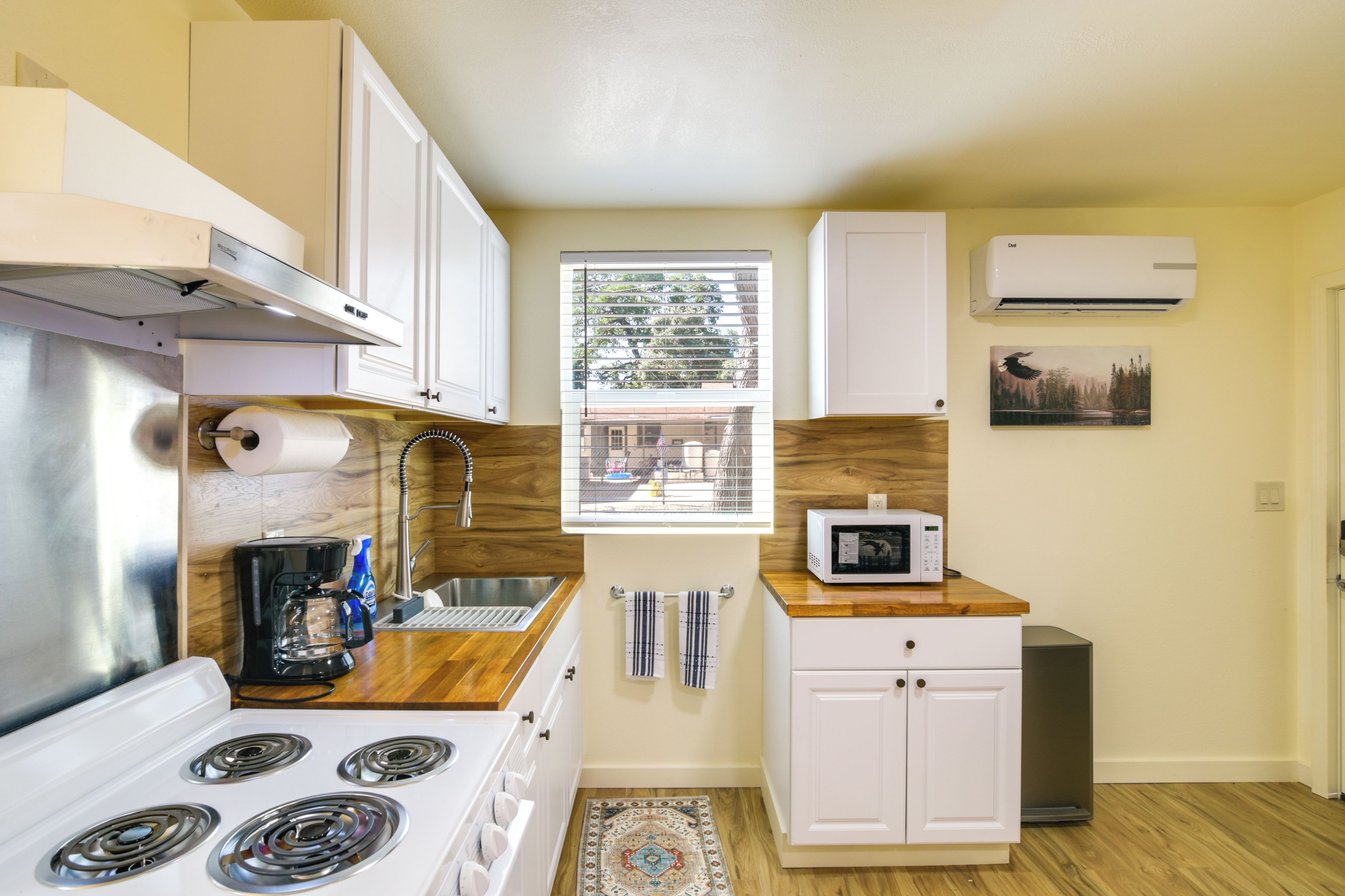 A compact kitchen with a stove, microwave, and a window with blinds.