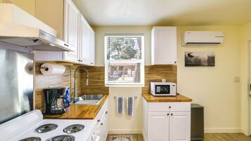A compact kitchen with a stove, microwave, and a window with blinds.