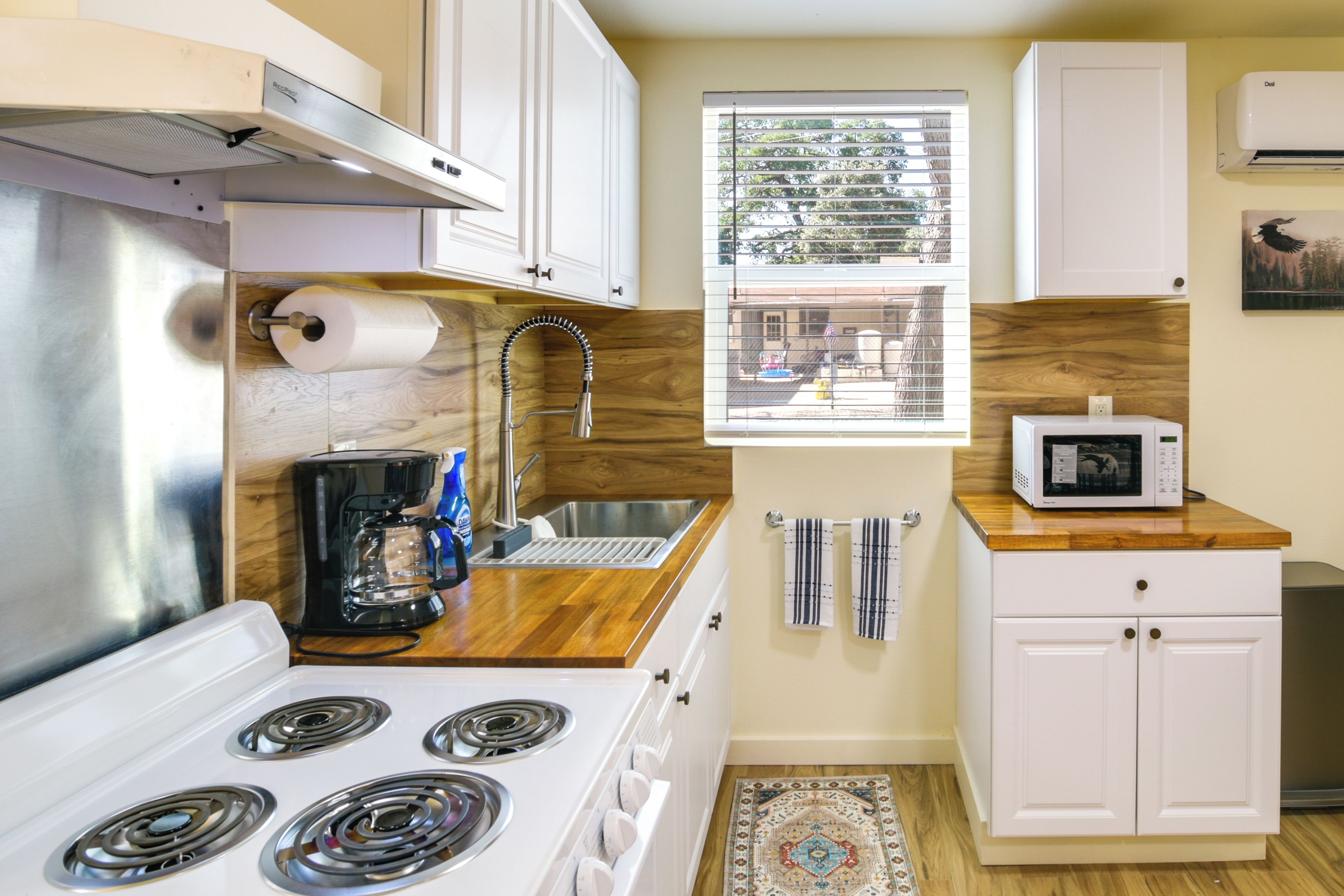 A compact kitchen with a stove, sink, and microwave, wooden countertops, and a window with a view.