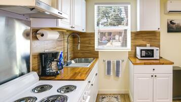 A compact kitchen with a stove, sink, and microwave, wooden countertops, and a window with a view.