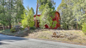 A red building surrounded by trees, with a clear sky and a road in the foreground. - Across From Hiking Trails: Woodsy Studio! (Idyllwild)
