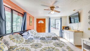 A bedroom with a large bed, a ceiling fan, a TV mounted on the wall, and a view of the outdoors through the window. - Across From Hiking Trails: Woodsy Studio! (Idyllwild)