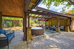 An outdoor patio with a covered seating area, a hot tub, and stone accents.