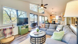 A spacious living room with a large flat-screen TV, a sofa, and a coffee table. There is a ceiling fan, large windows, and a kitchen in the background. - Dock on Hiwassee Lake! Family Murphy Retreat (Murphy)