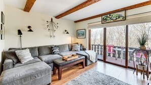 Un soggiorno con un divano ad angolo grigio, un tavolino in legno e un'ampia finestra con vista su un balcone.