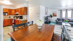 Een moderne keuken met houten kastjes, een eettafel met stoelen, een kroonluchter, en een zithoek met een bank en een salontafel.