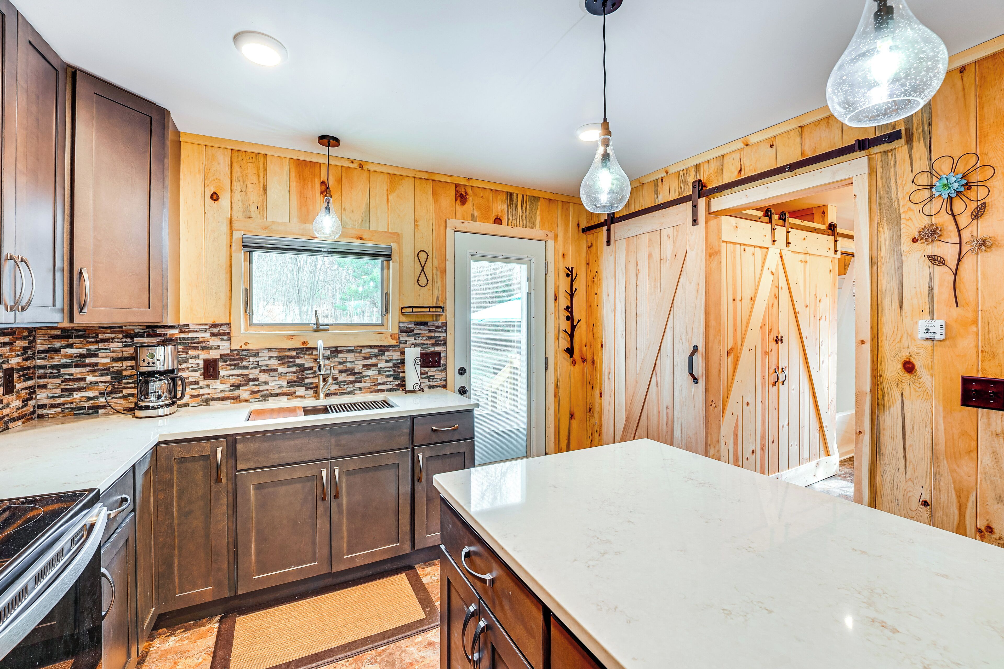 A kitchen with wooden cabinets, a marble countertop, and pendant lighting.
